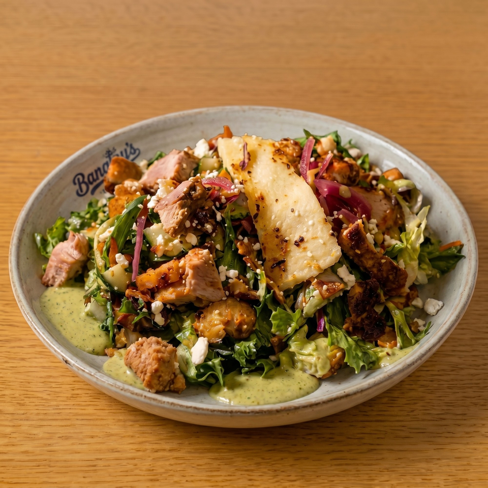 A Bananas restaurant salad with chicken, lettuce, feta, pickled onions, and green dressing on a wooden table.