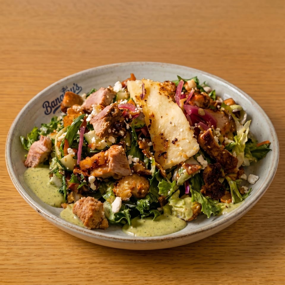 A Bananas restaurant salad with chicken, lettuce, feta, pickled onions, and green dressing on a wooden table.