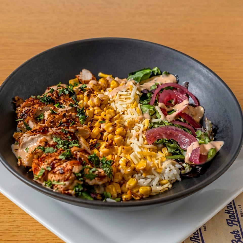 A black bowl filled with grilled chicken, corn, rice, shredded cheese, and red onion salad.