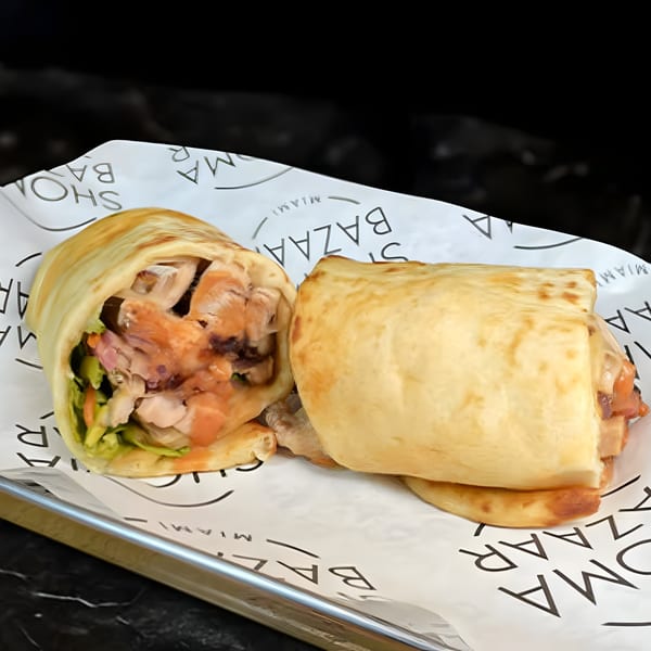 Two Chick N Jones wraps, one cut in half, filled with chicken and vegetables on branded paper.