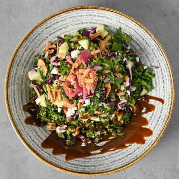 Overhead view of a colorful salad with greens, cheese, cucumbers, and dressing on a gray plate.