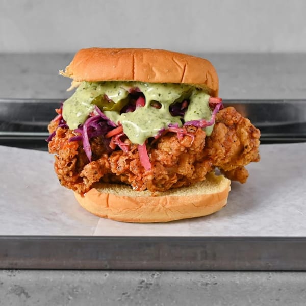Crispy fried chicken sandwich with green sauce, red cabbage, and pickles on a bun.