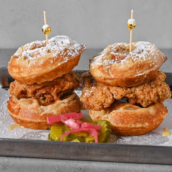 Two Chick N Jones chicken and waffle sliders with powdered sugar, honey, and pickled vegetables.