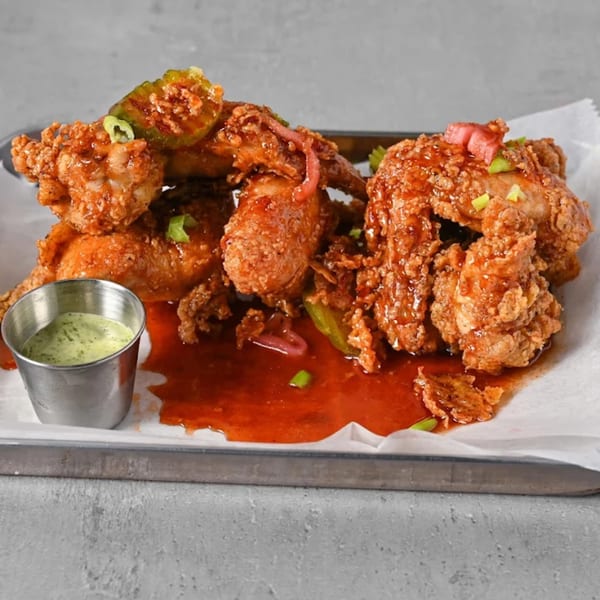 Crispy Chick N Jones wings, drenched in red sauce, with green onions, pickles, and a side of green dip.